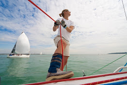 Woman leaning off a sailboat holding onto a rope with water and sky behind her